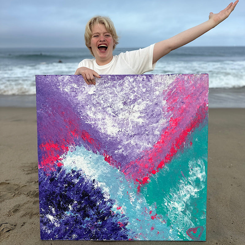 Pacific, Original by Clara Woods — Clara at the beach holding the Pacific painting upright in the sand, smiling, with the ocean behind her