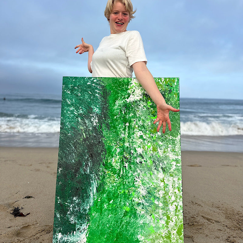 Atlantic, Original by Clara Woods — Clara at the beach holding the Atlantic painting upright in the sand, laughing, with the Pacific Ocean behind her