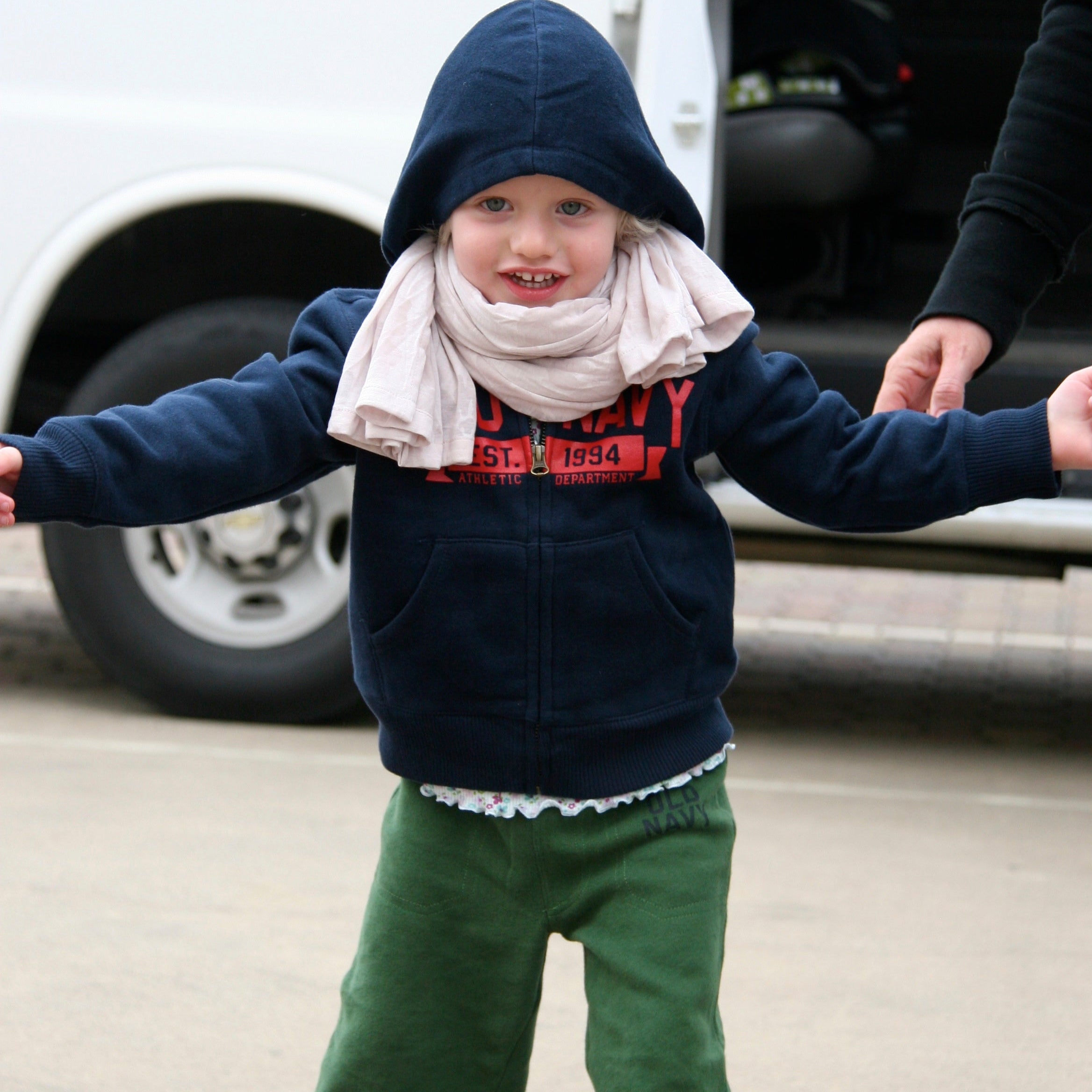 Child wearing a navy blue hoodie and green pants with a white vehicle in the background
