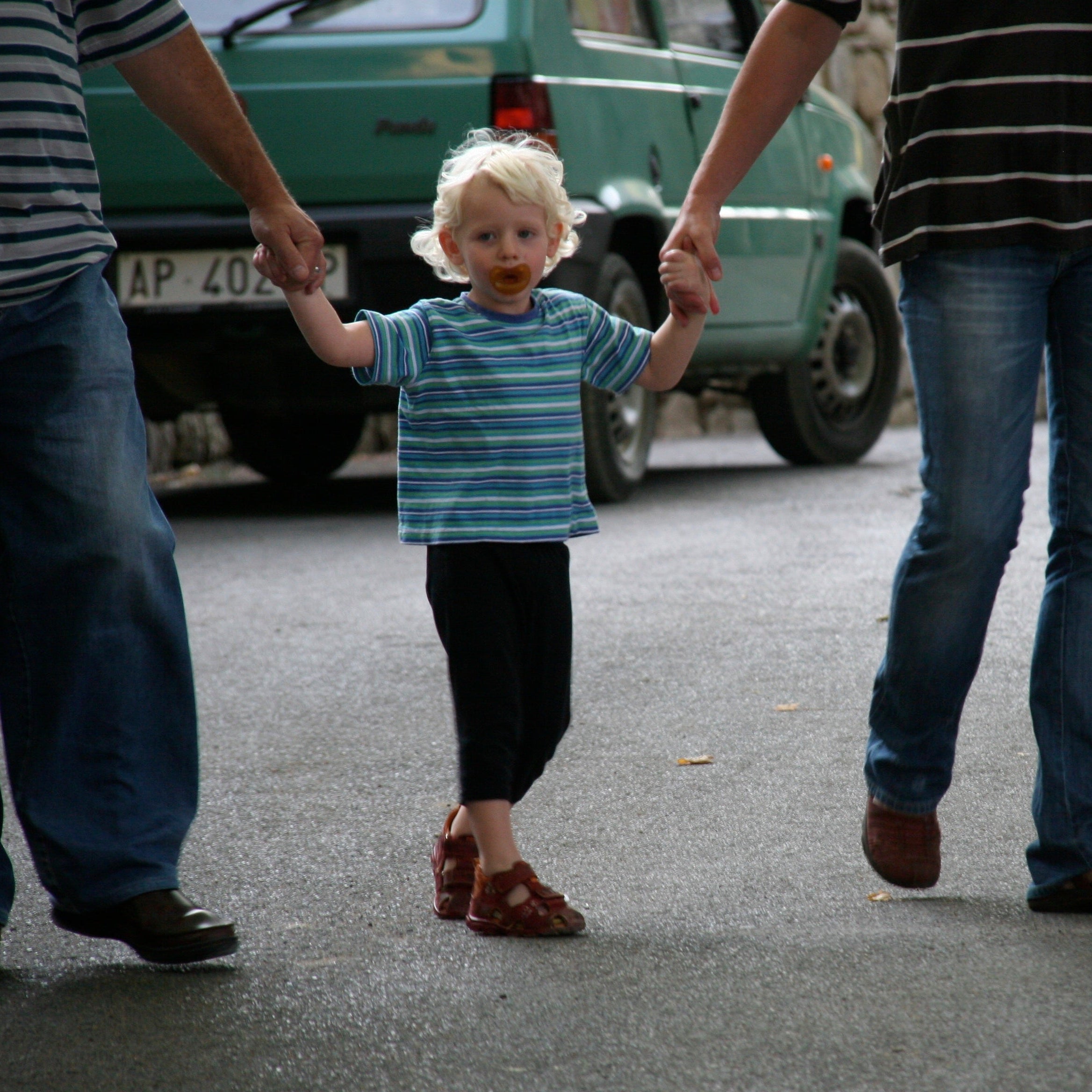 Two adults holding hands with a young child on a street.